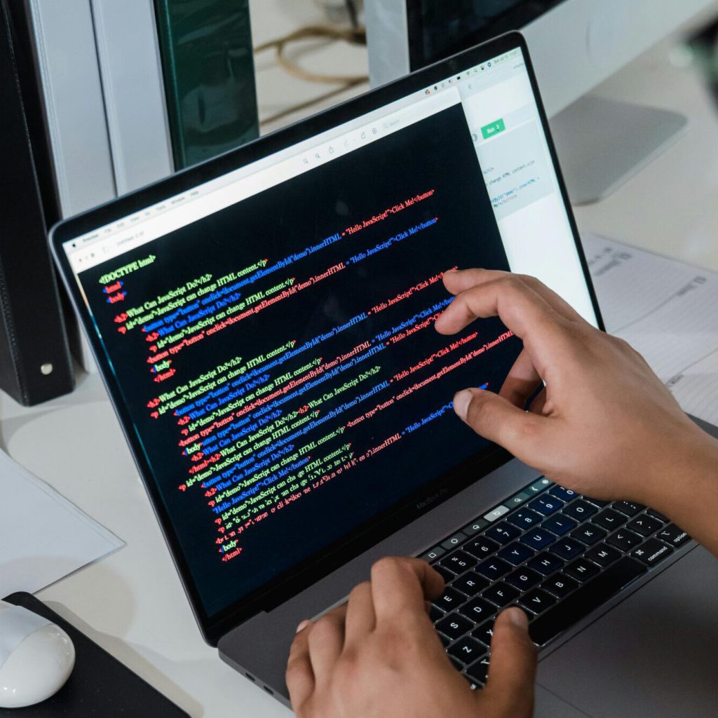 Close-up of a programmer pointing at a colorful code script on a laptop in an office setting.